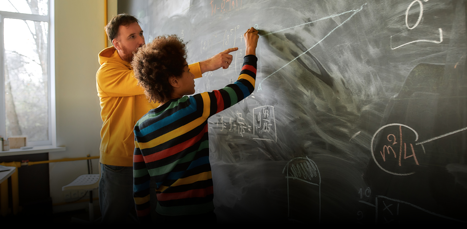 Image of a teacher working with a young student on a geometry problem in front of a blackboard