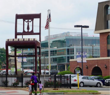 Image of the Anacostia Professional Building with a family walking in front. In the parking lot is a large chair that is as tall as a building.